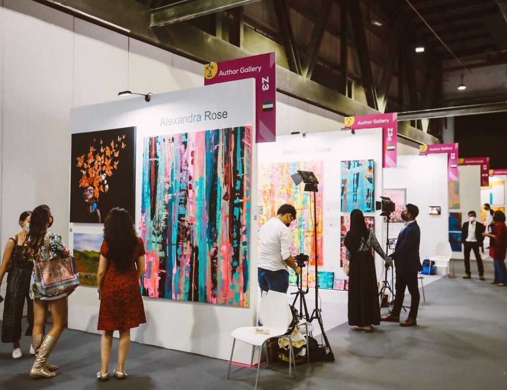 "Colorful abstract painting displayed at World Art Dubai exhibition in a large hall. The painting features vibrant shades of blue, green, pink, and yellow, creating a unique and eye-catching composition.