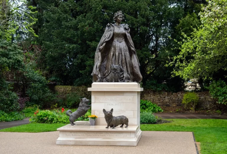 Bronze statue of Queen Elizabeth II in regal attire, accompanied by three corgis at her feet, Oakham's tribute to the monarch's enduring legacy.